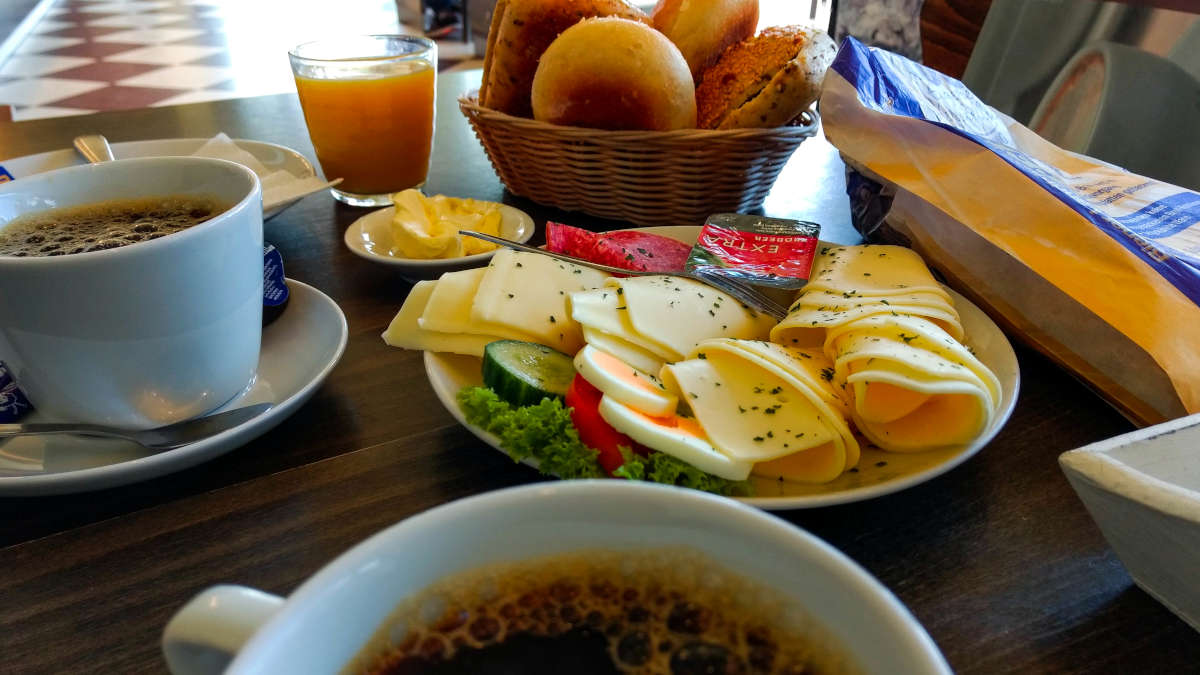 German breakfast: coffee, plate of cheese, sliced egg and veggies plus a basket of bread rolls