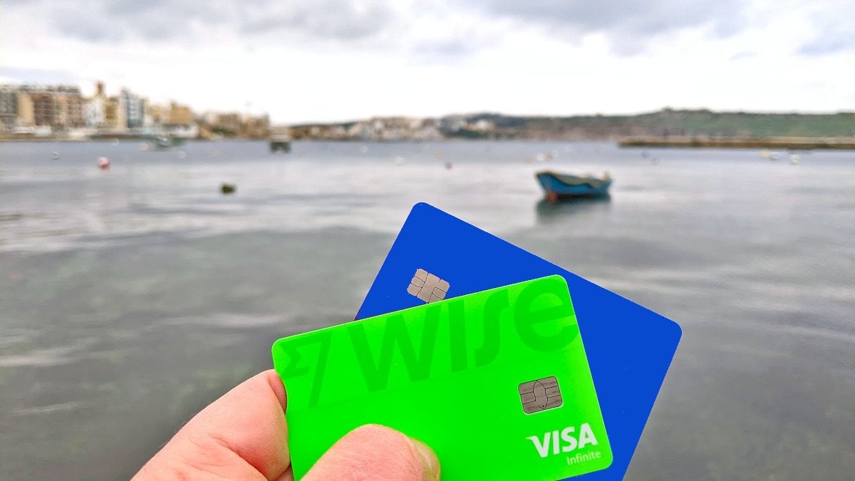 A hand holding up travel payment cards with Malta scenery in the background