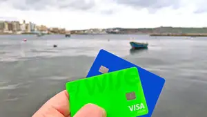 A hand holding up travel payment cards with Malta scenery in the background