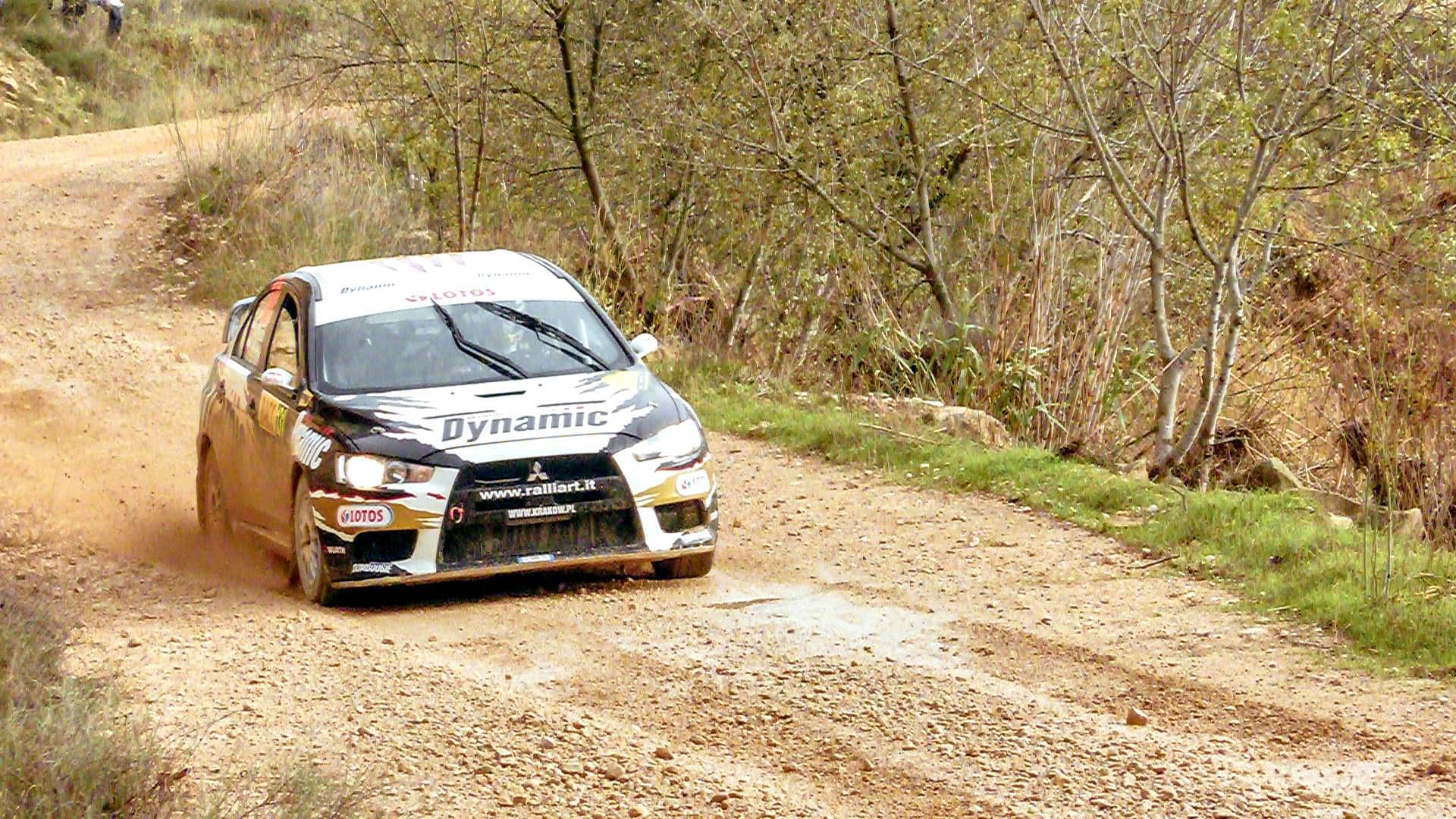 WRC rally car on a dusty road in Spain. The car just came around the bend, on the straight now