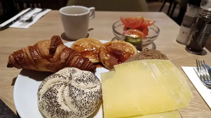 Close-up of my breakfast plate: bread roll, croissant, cheese and a tiny salad selection