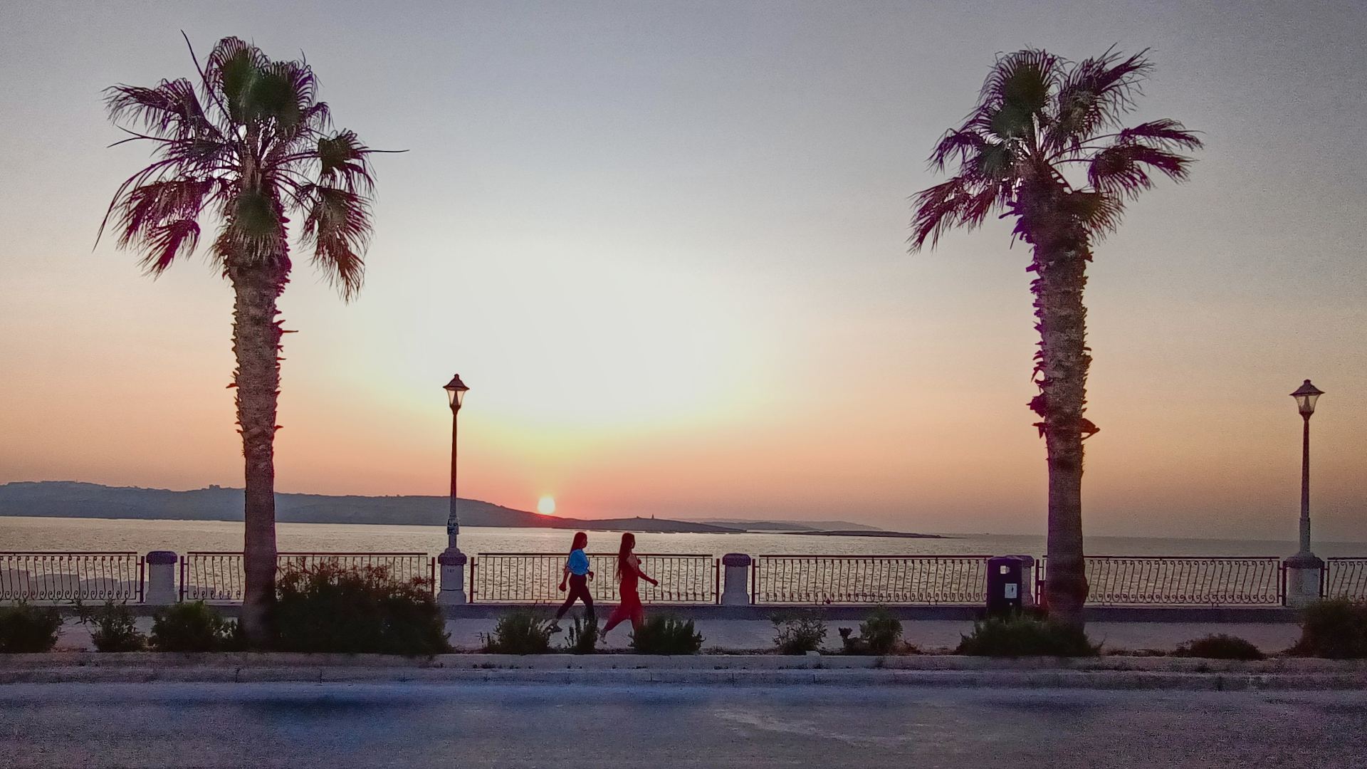 Sunset on Malta boulevard: two palm trees and two people walking by