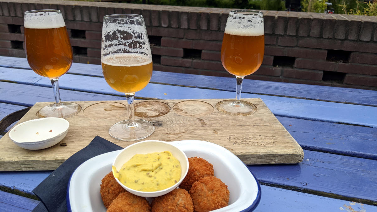 3 glasses of beer (tasting flight) on a blue table with a bowl of bitterballen and mustard in front of it