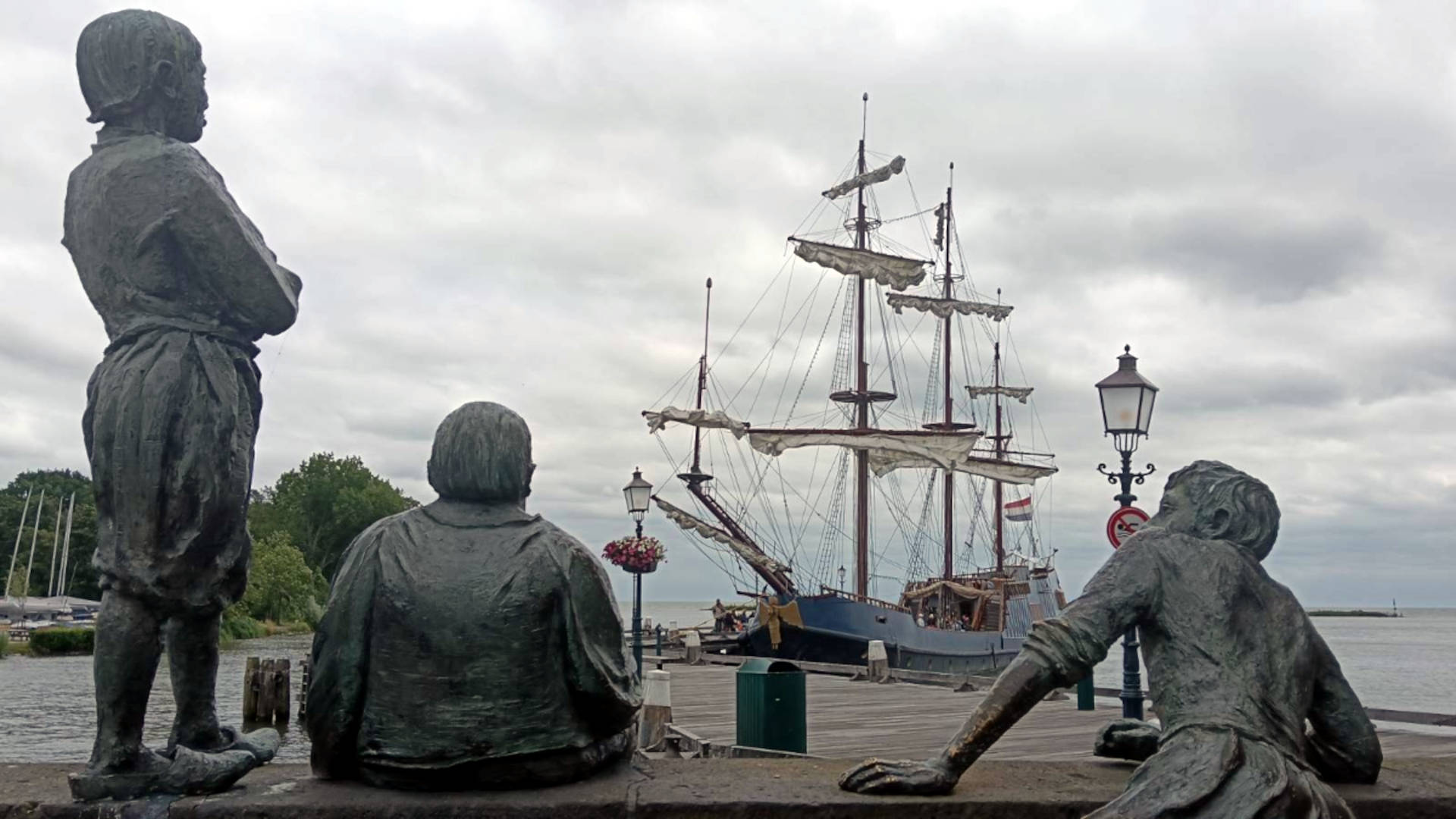 Jongens van de Bontekoe statues seen from behind, looking over the water - Sailing boat in the distance. Cloudy day.