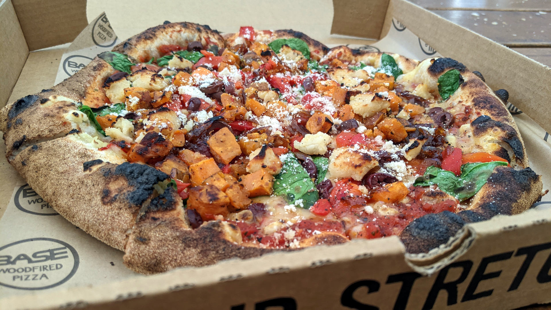 Handmade wood-fired pizza hot out of the oven (in a cardboard take-away box)