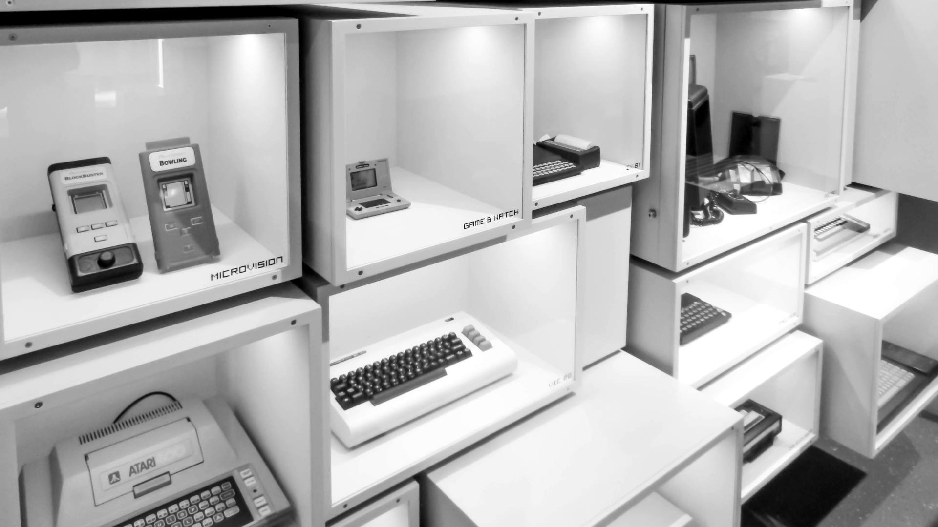Classic computers and game console on exhibit in square diplay cases