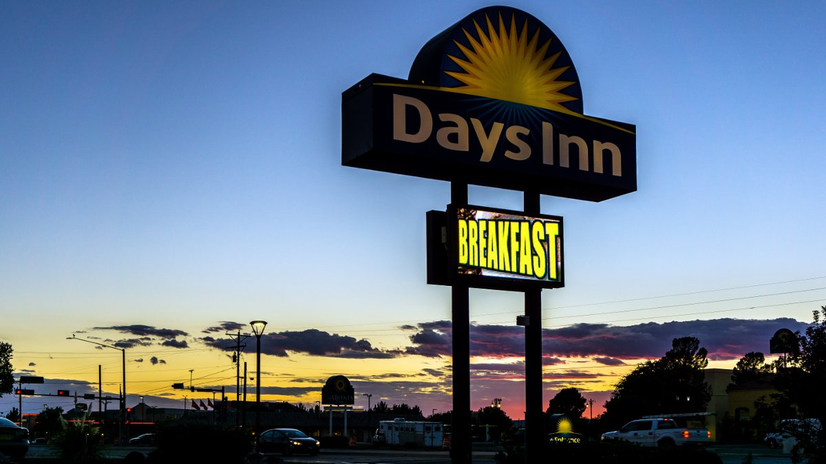 Days Inn motel sign in centre, sun is setting, ciry and cars in background