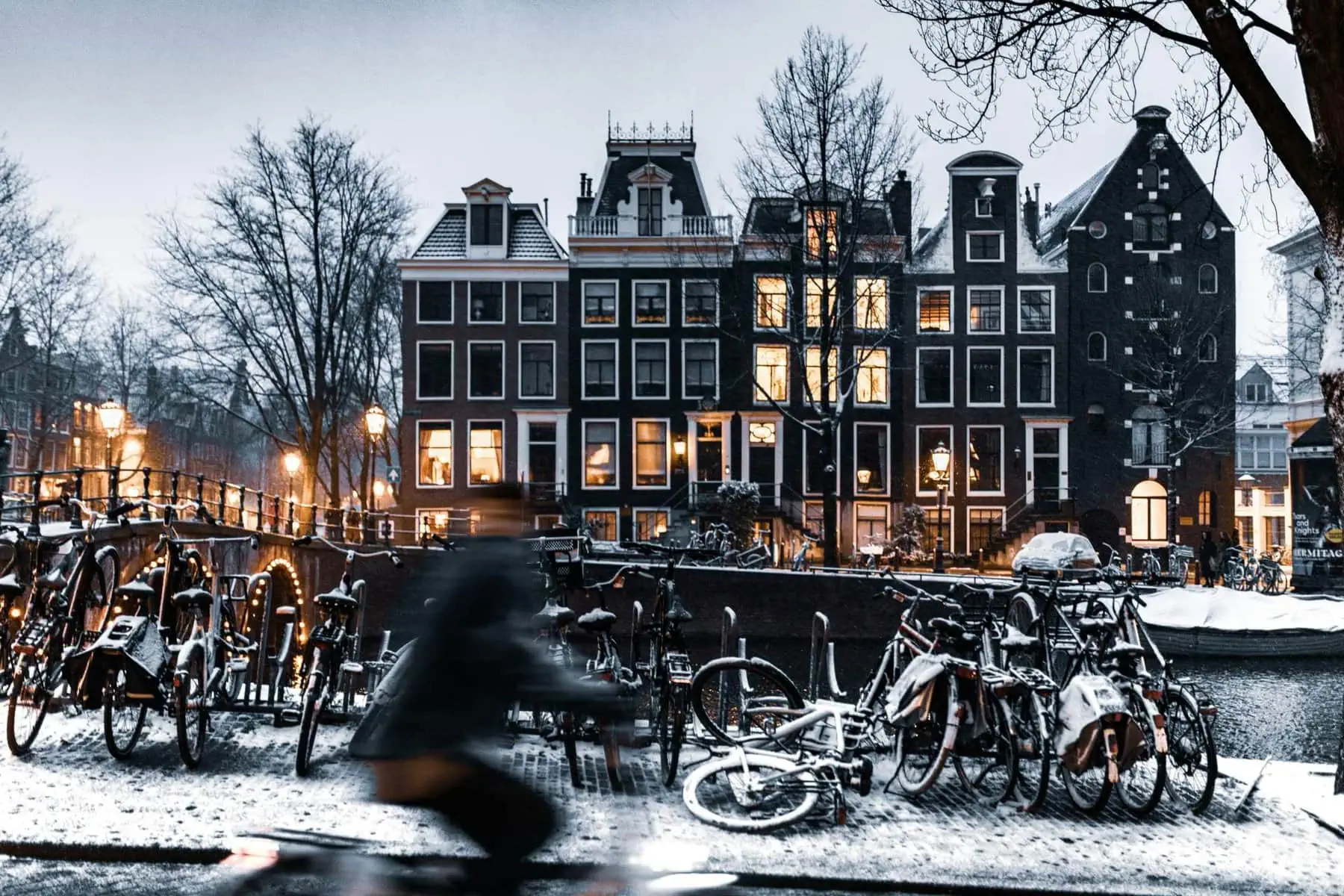 Photo of Amsterdam in winter - a bit snowy. Houses in the distance, cyclist passing by in the foreground