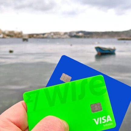 A hand holding up travel payment cards with Malta scenery in the background